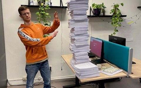 Op de foto liggen op een tafel de 113 dagvaardingen opgestapeld. Naast deze stapel staat een werknemer van !WOON.