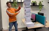 Op de foto liggen op een tafel de 113 dagvaardingen opgestapeld. Naast deze stapel staat een werknemer van !WOON.